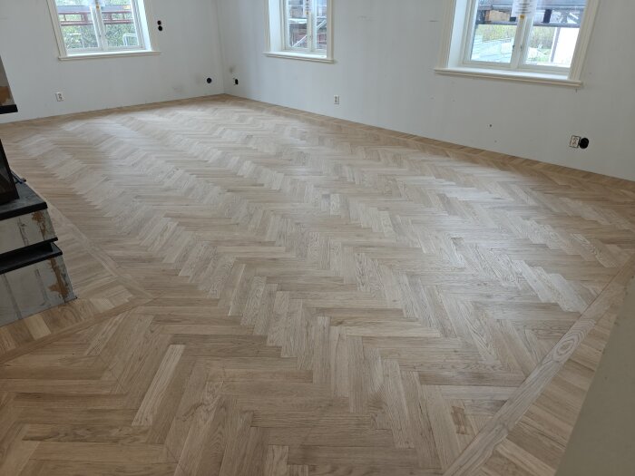 Nyparkett lagd i ett rum med stora fönster, visande fiskbensmönster på golvet med ljusinsläpp från två håll.