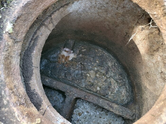 Brunnens insida med slam och rör, visar möjligt behov av tömning. Avloppssystemet i fråga om tömning och funktion diskuteras.