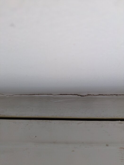 Sprickor i vitt fönsterkarm där både färg och troligen betong har spruckit.