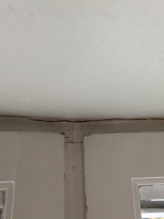 Sprickor i vitmålad fönsterkarm och vägg med flagnande färg och skadad betong.