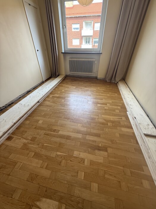 Ljust trägolv i fiskbensmönster i ett rum med beige väggar och stort fönster.