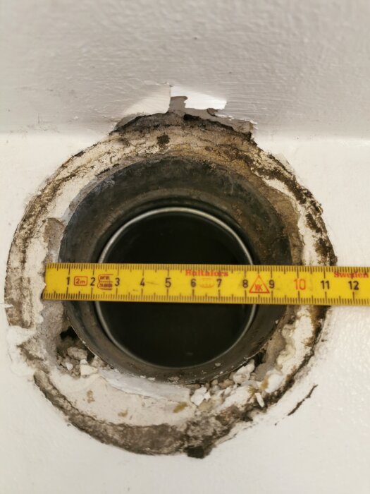 Gammalt frånluftsdon med måttband ovanpå, visar väggsläpp runt hålet.