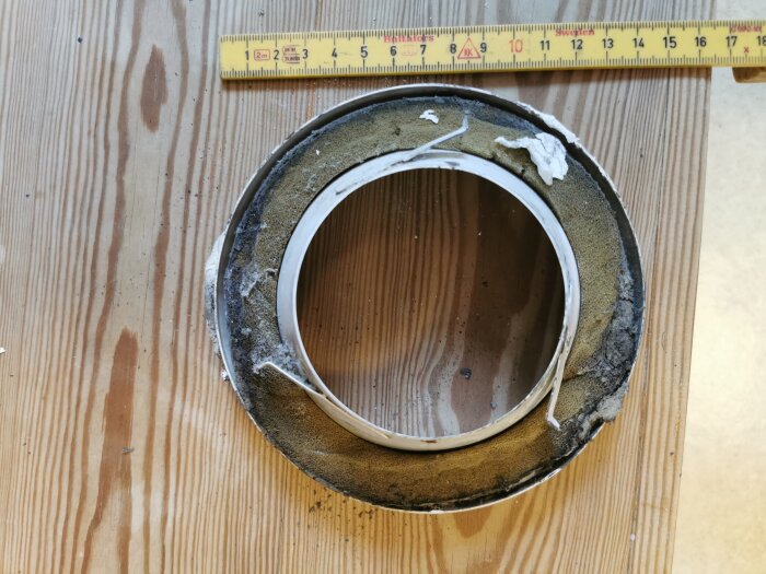 Gammalt frånluftsdon med mått i centimeter visat på träbord, belagt med smuts och damm, bredvid måttstock.