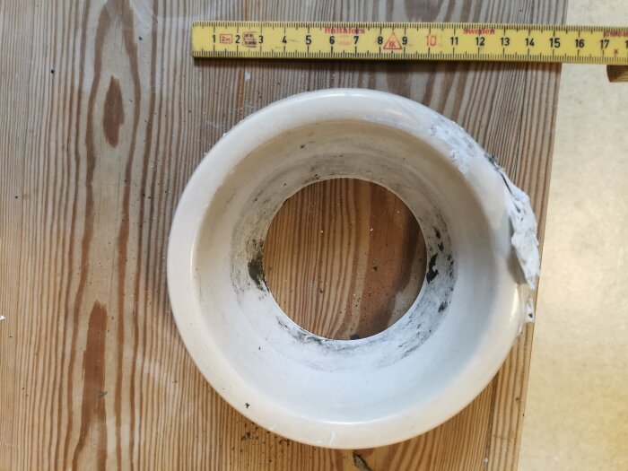 Gammalt plastfrånluftsdon placerat på trägolv, smutsigt och delvis skadat, med tumstock i bakgrunden för att visa mått.