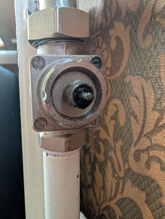 Läckande packbox med synlig pigg på rör mot mönstrad vägg.