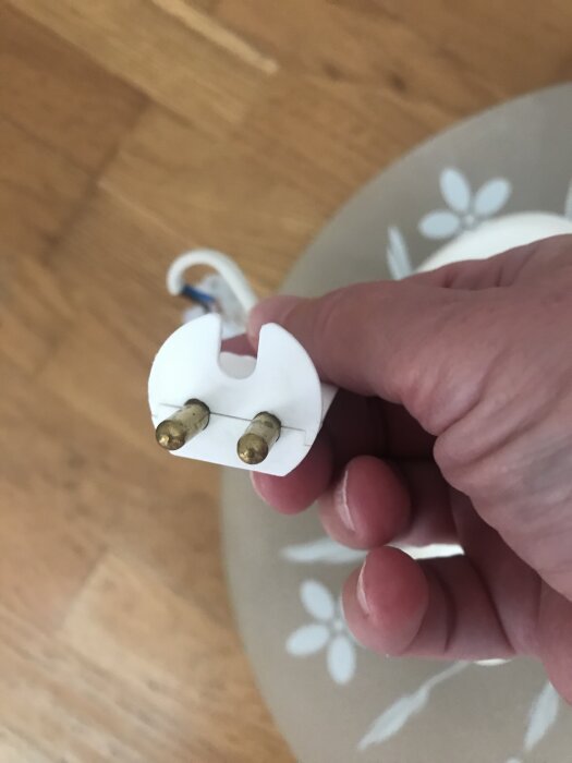 En hand håller i en lampa med en vit plugg och två metallstift.