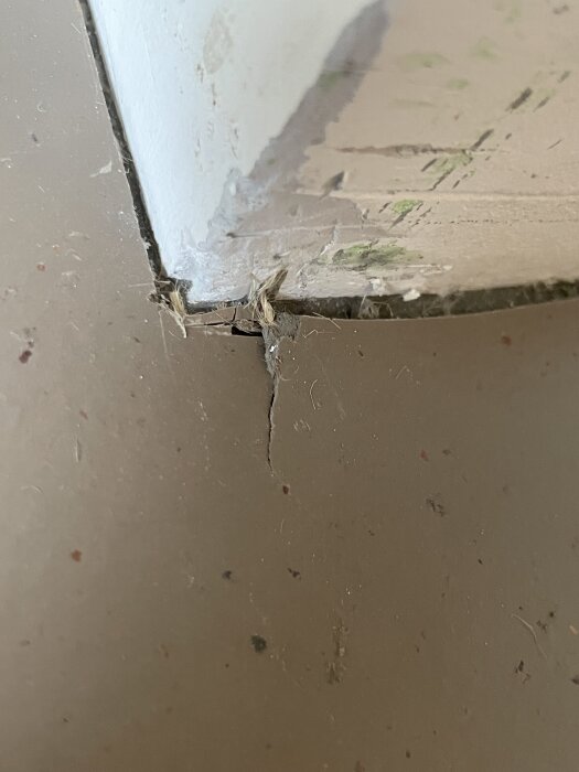 Spricka i linoleumgolv i hörn, med fransig kant och ojämnt utfört arbete.