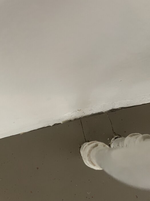 Spricka i linoleummatta vid golvhörn, synliga svetsskarvar och en upprullad matta vid ett rör.