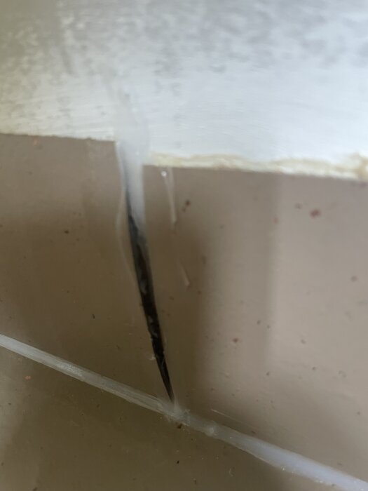 Close-up av en skadad linoleummatta med en spricka i hörnet där mattan har spruckit, synliga repor och dåligt utförd svetsskarv.