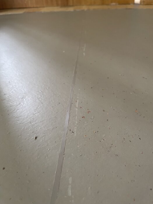 Linoleummatta med synlig svetsskarv och ytliga repor, antydande slarvigt utförd golvläggning på grått golv.