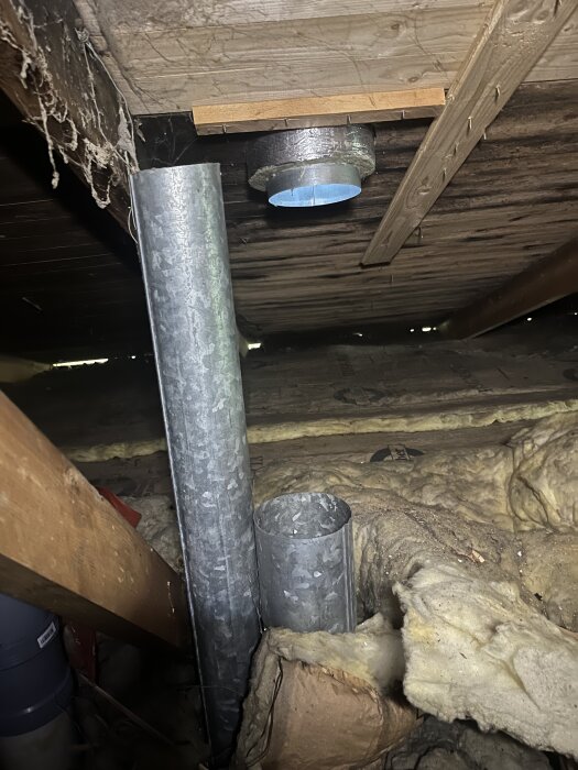 Ventilationsrör i en kallvind, omgiven av isolering. Det syns en öppning i taket där fuktig luft har blåst ut.