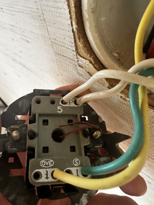 Närbild av en elektrisk strömbrytare med kablar av olika färger anslutna, mot en vit vägg.