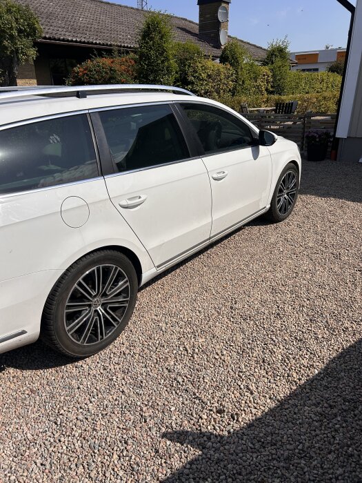 Vit kombibil med nyinstallerade 18-tumsfälgar och svarta däck, parkerad på en grusuppfart framför ett hus med trädgård.