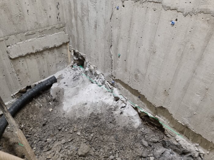 Betongvägg med spricka vid basen, omgiven av jord och ett svart dräneringsrör.