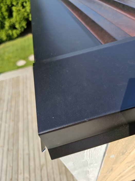 Svart plåtgavelbeslag provisoriskt placerad, ovanpå ny fasad som når taket, saknar vindskivor, mot en bakgrund av trätrall och gräsmatta.