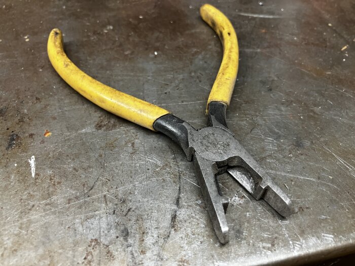 Gulhandtagad tång med en unik, avrundad spets och avbitarfunktion på ett metallunderlag.