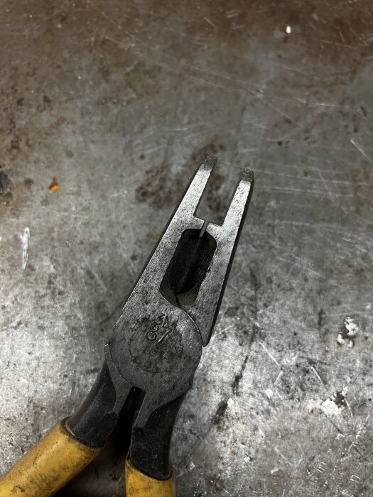 Specialiserad tång med gul handtag och avrundad spets, som lämnar ett mellanrum när stängd. Används för oklar funktion.