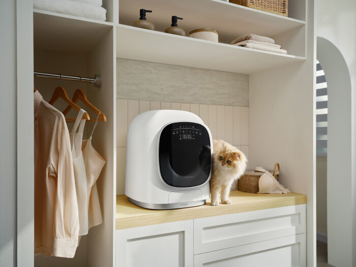 Kompakt Roborock ZEO Mini tvättmaskin i ett stiligt tvättrum, med en katt stående bredvid, omgiven av hyllor med handdukar och korgar.