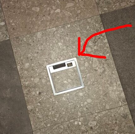 Upptagen lucka på golv med kakelplattor, röd pil pekar mot rektangulärt hål.
