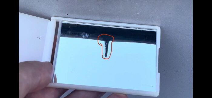 Närbild av en inringad komponent i ett byggprojekt, hålls mot en reflekterande yta, relaterad till diskussion om läckagerisker och kapillärt flöde.