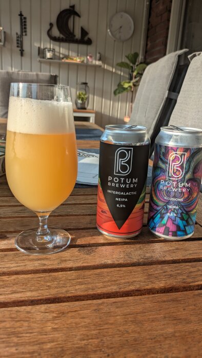 Ett glas skummande öl bredvid burkar från Potum Brewery, placerade på ett träbord i en solig inomhusmiljö.