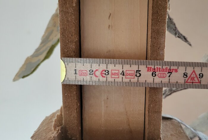 Närbild av en träfiberskiva och regel med ett måttband som visar tjockleken på skivan.