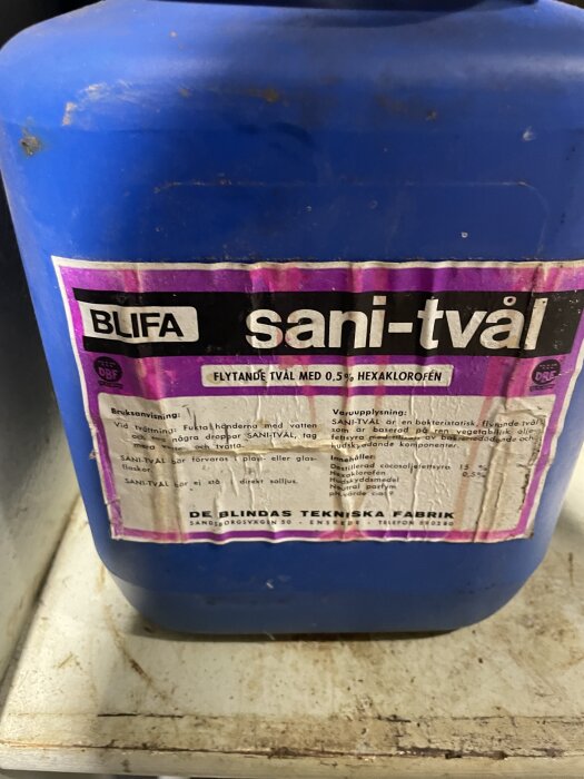 En blå behållare med etikett för BLIFA sani-tvål, flytande tvål med 0,5% hexaklorofen, från De Blindas Tekniska Fabrik.