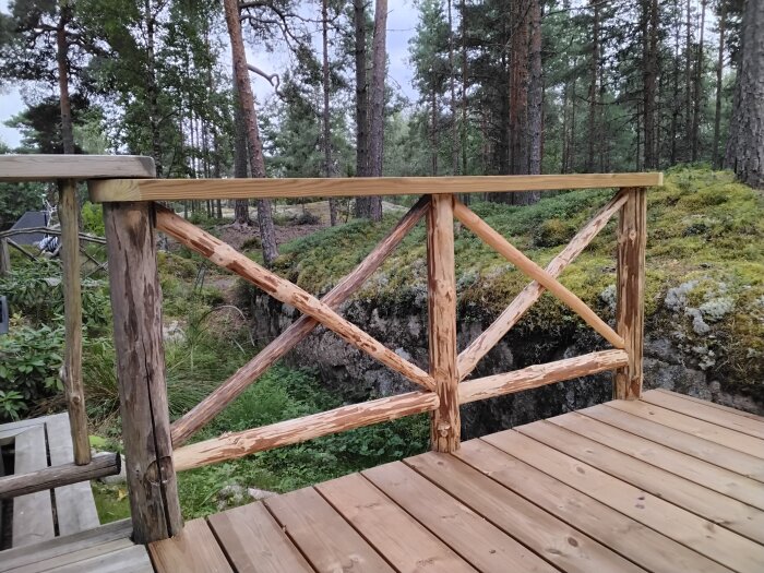 Träräcke på terrass med tall, gran och rönn med utsikt över en klyfta, omgiven av skog och mossa.