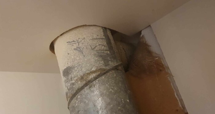 Ett ventilationsrör med synliga skador och smuts mot ett tak hörn i ett kök, möjligt fel på spisfläktsinstallation.