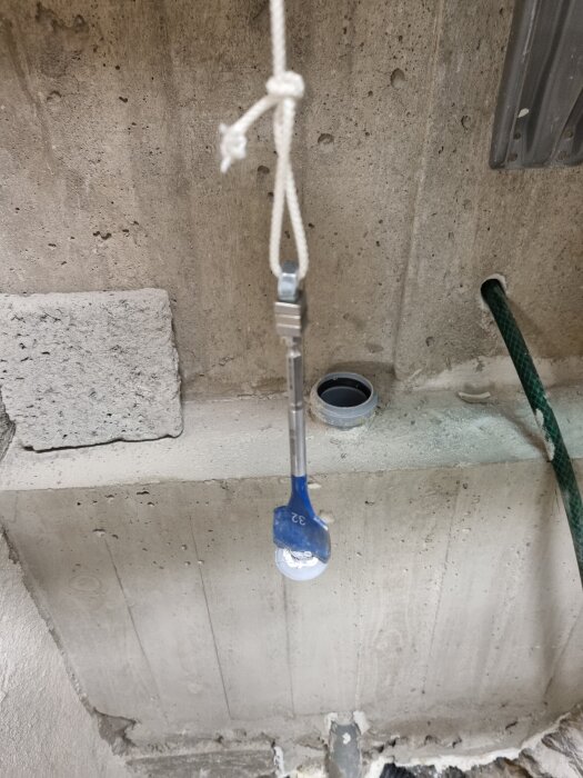 Betongvägg med hål och ett borr på ett snöre.