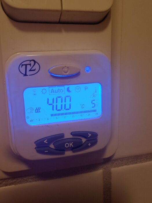 Display av en T2 termostat som visar 40,0°C med blå bakgrundsbelysning, flera ikoner synliga, knappar för justering nedan.