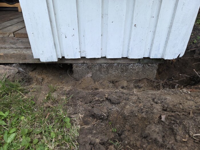 Utgrävd mark runt bod med synliga plintar och sand, trasig regel planeras bytas ut, diskussion om val av fyllnadsmaterial.