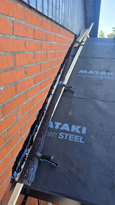 Tegelvägg med takplåt och tätskikt installerat, Mataki Haloten Steel synligt. Asfaltskit använt för tätning mot väggen.