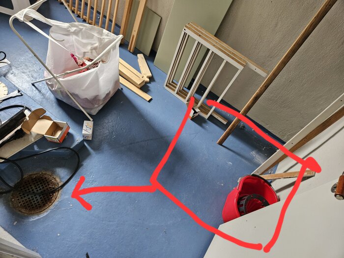 Bild av ett rum med blått golv, bråte och en golvbrunn i gjutjärn. En röd markering visar plats för en planerad dusch.