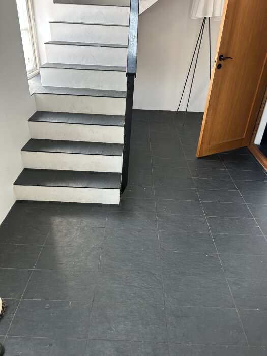 Trappor och golv i hall med kluven lerskiffer, vägg och dörr synliga. Diskussion om ytbehandling för enklare rengöring utan blankt utseende.