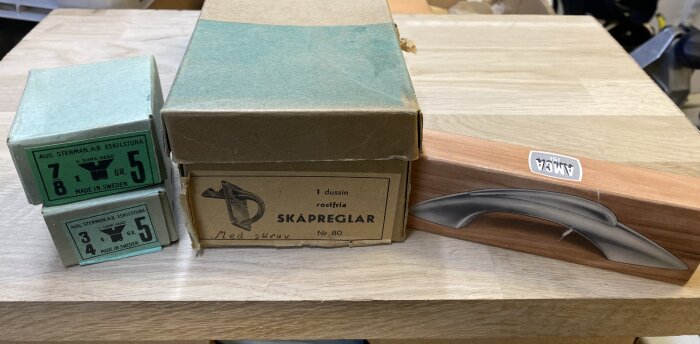 Kartonger med skruvar och skåpreglar på ett bord. En grön kartong från Eskilstuna och en större brun kartong märkt "Skåpreglar".