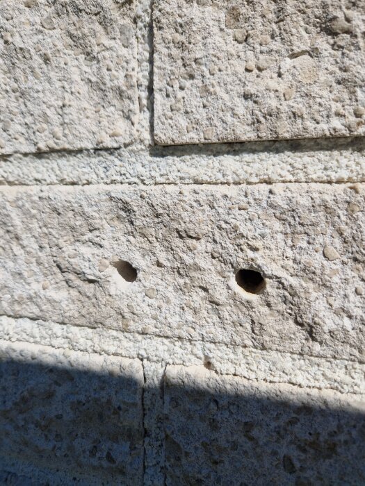 Borrhål i beige tegelvägg efter borttagna fästen för tv-antenn och parabol.