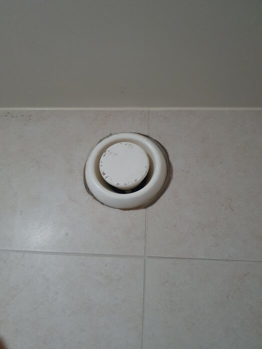 Ventilationslucka i taket med lite smuts runt kanterna, verkar gammal och del av en större ventilationssystem i byggnaden.