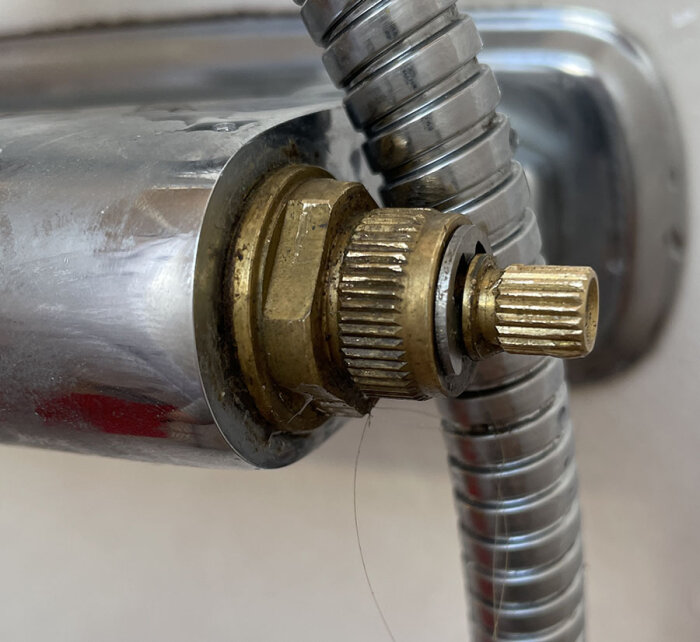 Närbild av en del i en blandare med mässingdetaljer och en flexibel metallslang, del av ett värmereglerande system för vatten.