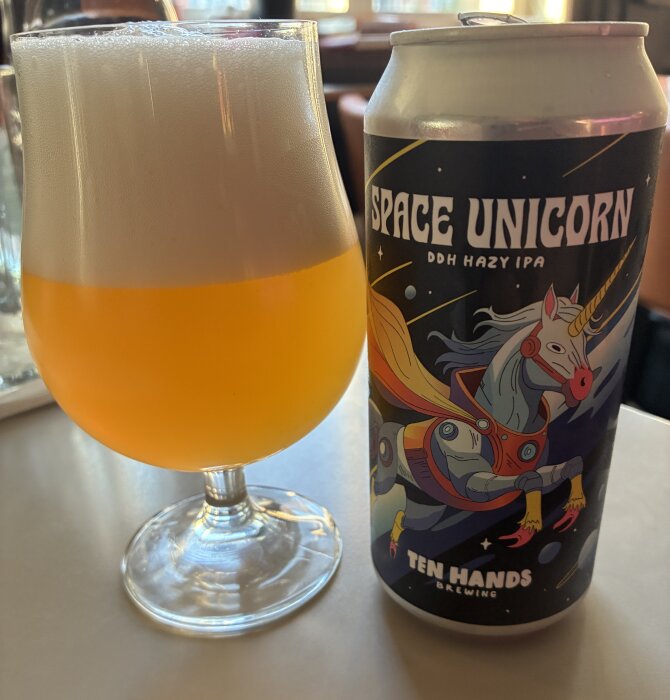 Ett glas öl bredvid en burk med etiketten "Space Unicorn DDH Hazy IPA" från Ten Hands Brewing, illustrerad med en rymdfärgad enhörning.