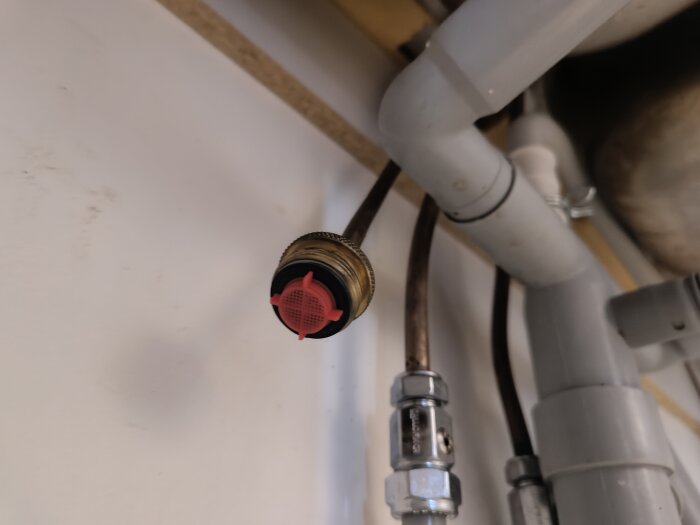 Diskbänksanslutning med rör och kopplingar, där en röd komponent blockeras och hindrar gängning av diskmaskinens slang till blandarens ledning.