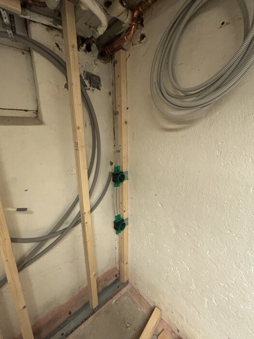Träram med gröna fästen för eluttag på vägg, rör och kablar i hörn av renoveringsprojekt.