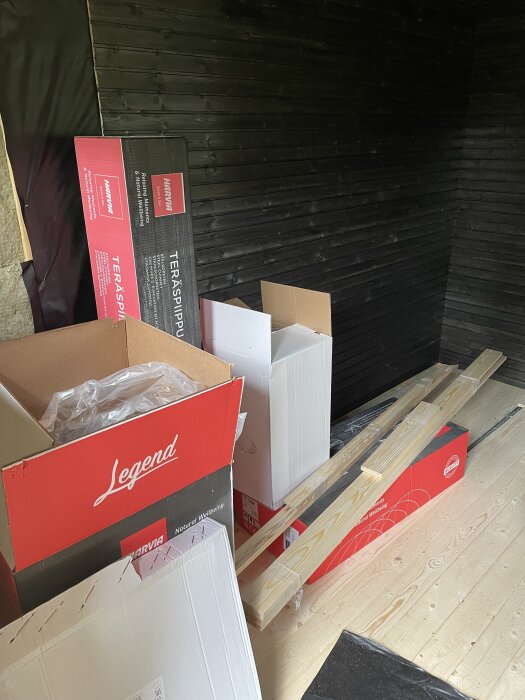 Kartonger och träplankor på ett nylagt golv i en bastu under konstruktion.