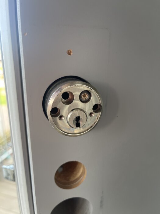 Cylindrisk dörrlåsmekanism med skador runt mässingskulor. En borrknäckning syns, vilket gjort utvinningen av kulorna svårare.