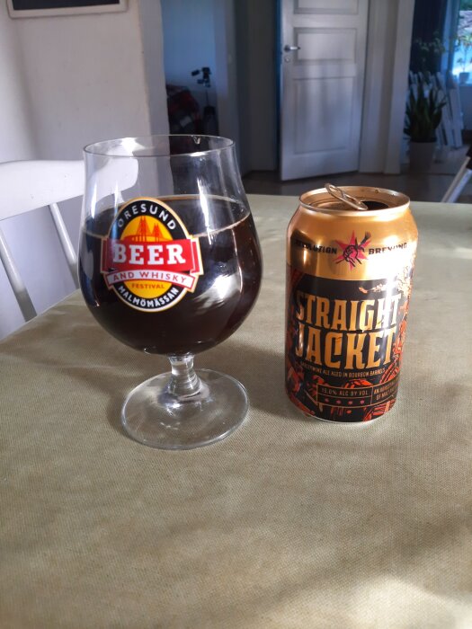 Ett glas med mörk dryck och en ölburk märkt "Straight Jacket" på ett bord.