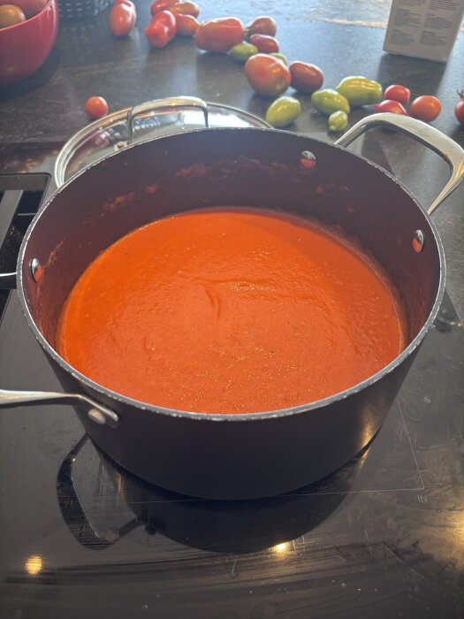 Kastrull med röd tomatsås på spisen, omgiven av färska tomater i olika färger på bänken.