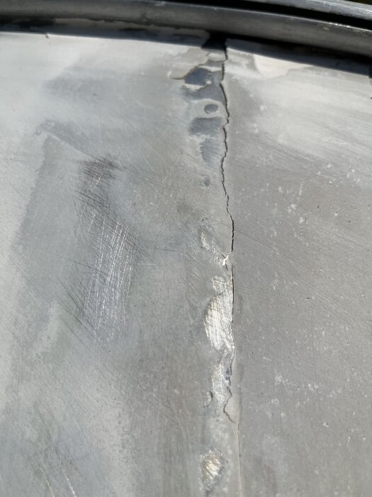 Sprucken skarv mellan aluminiumplåtar med synliga ytskador, troligen orsakad av termisk expansion och väderpåverkan.