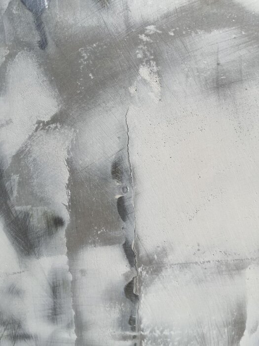 Spricka i spacklad yta mellan aluminiumplåtar med synliga borstningsmärken och färgrester, indikerar kosmetiska fel och behov av reparation.