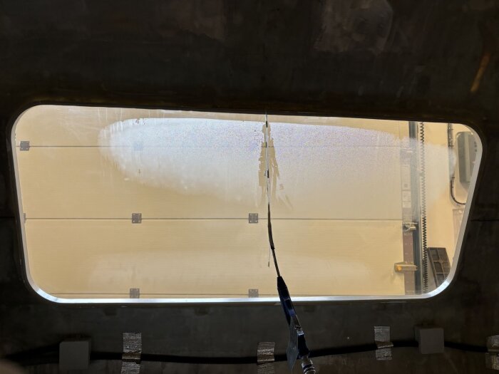 Fönster med pågående avfuktning, synlig kondens minskar från botten där en slang för in torr luft för att lösa fuktproblem.