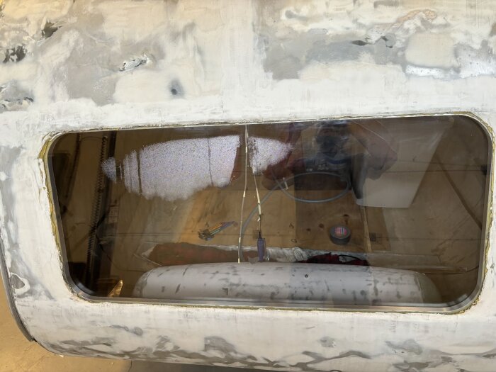 Vintagevagn med pågående fönsterlagning; spacklade ytor runt fönster, apparat, tapetkniv och tejp inuti vagnen.